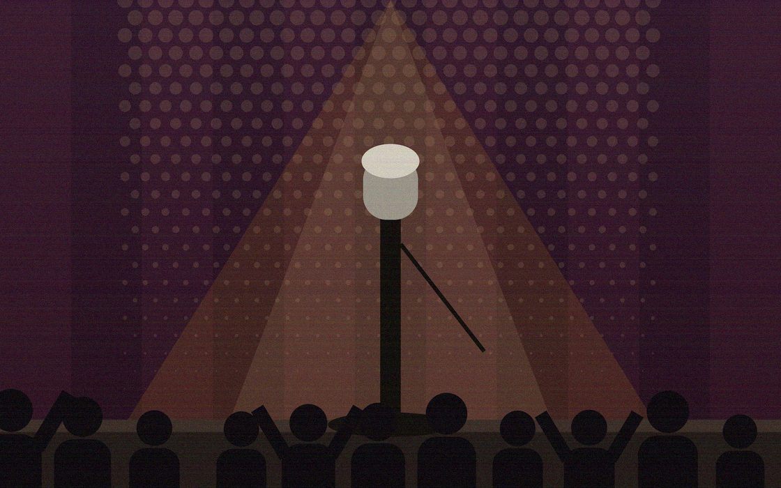 A performer at the microphone on a small club stage in front of a full room